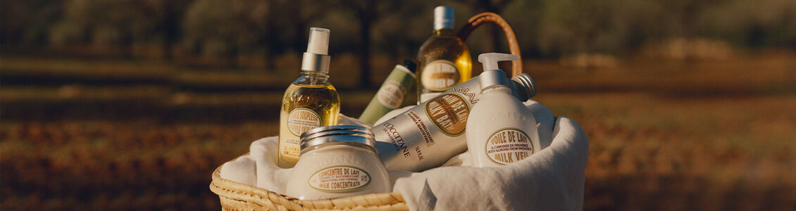 Almond collection of L'Occitane bath, shower and body products in a woven basket in the field