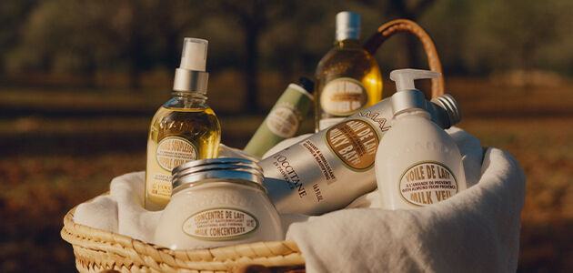 Almond collection of L'Occitane bath, shower and body products in a woven basket in the field